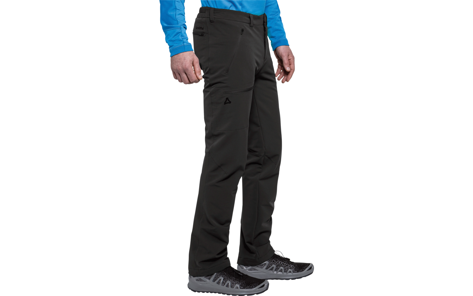 Parte inferior del cuerpo de una persona de pie con pantalones softshell negros, una prenda azul de manga larga y zapatillas de senderismo gris-negro; manos a los lados