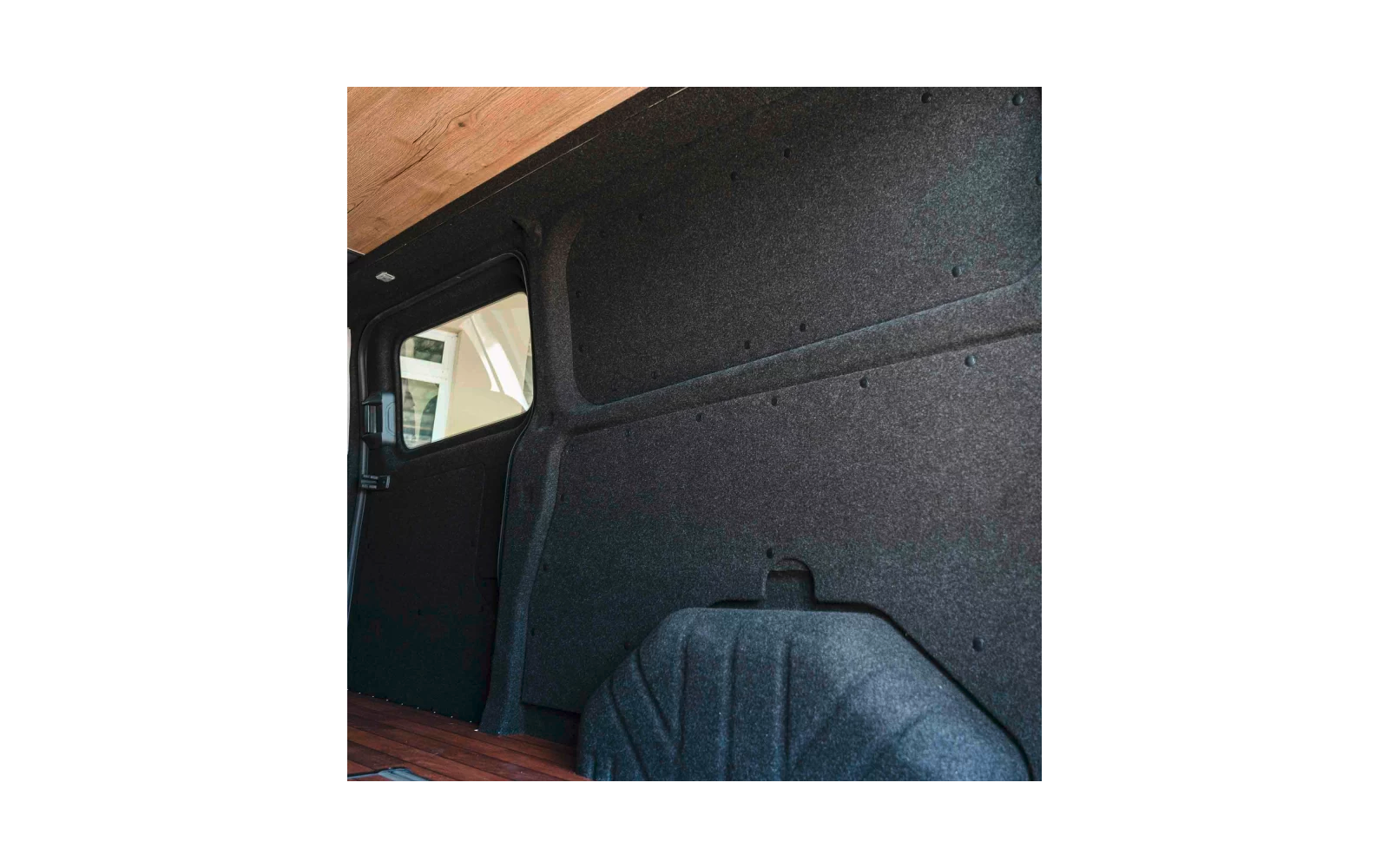 Innenraum eines Kastenwagens mit dunkelgrauer Wandverkleidung, sichtbarem Radkasten, Holzboden und kleinem Seitenfenster links