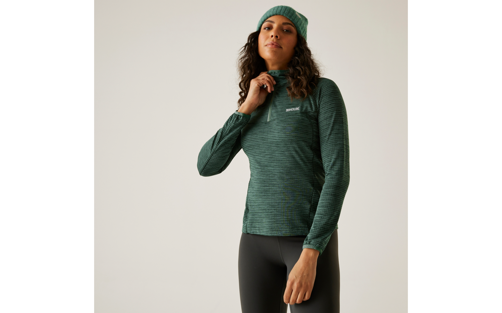 Femme portant un bonnet vert et un pull vert debout devant un fond clair