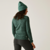 Femme vue de dos portant un pull vert, un legging noir et un bonnet vert sur un fond beige