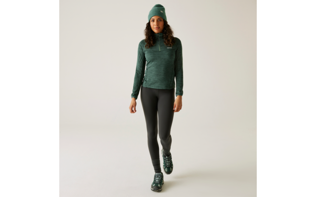 Femme en sweat à capuche vert, pantalon noir et chaussures sur fond beige