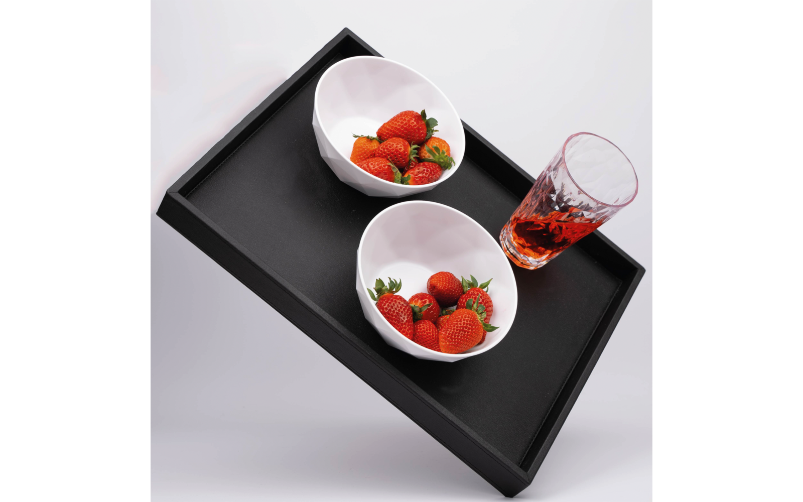 Schwarzes Tablett mit zwei weißen Schalen mit Erdbeeren und einem Glas mit roter Flüssigkeit