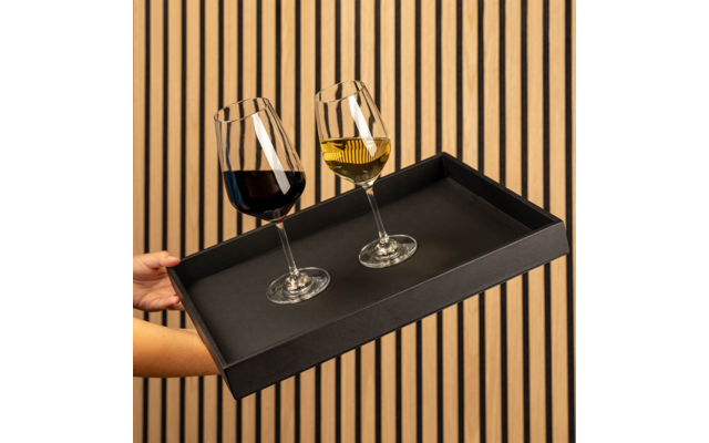 Hände halten schwarzes rechteckiges Tablett mit zwei Weingläsern (links Rotwein, rechts Weißwein) vor vertikaler Holzlattenwand