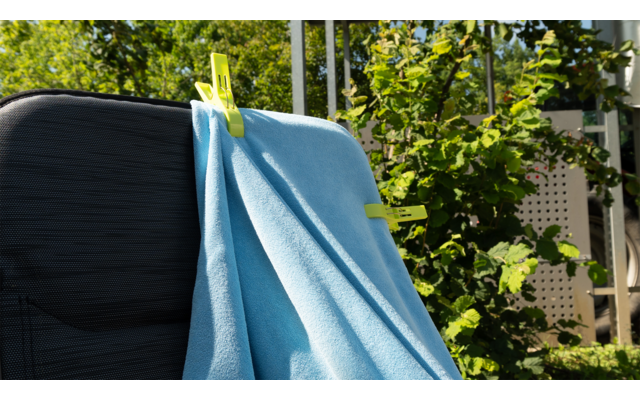 Blauer Pullover hängt an einer Wäscheleine im Freien, im Hintergrund Bäume und Sonnenschein