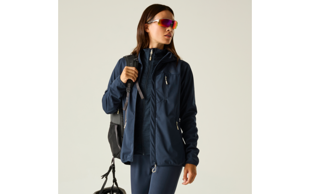 Persona con chaqueta outdoor azul oscuro y mochila, que sostiene un casco de bicicleta y lleva gafas de sol deportivas coloridas