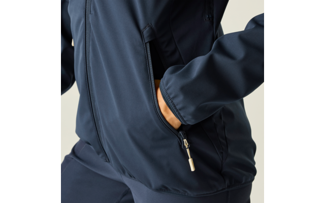 Primer plano del torso con chaqueta azul oscuro; mano derecha en el bolsillo lateral con cremallera, tirador metálico visible y puño elástico; cabeza no visible