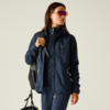 Persona con chaqueta outdoor azul oscuro y mochila, que sostiene un casco de bicicleta y lleva gafas de sol deportivas coloridas