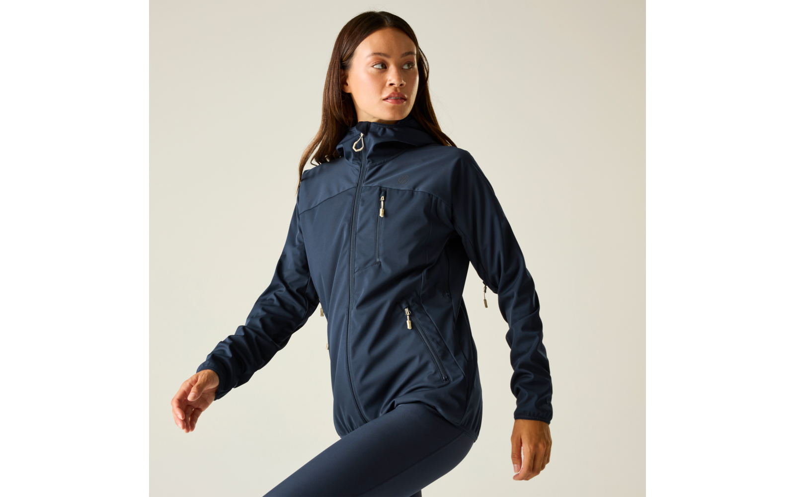 Mujer con chaqueta con capucha azul marino con bolsillos con cremallera y leggings azul marino, en postura de marcha frente a un fondo claro, mirando hacia la derecha