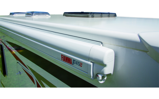 Roof of a white motorhome with two roof vents and a rolled-up awning labeled "Fiamma F45S", background shows a lake, trees and mountains under a blue sky