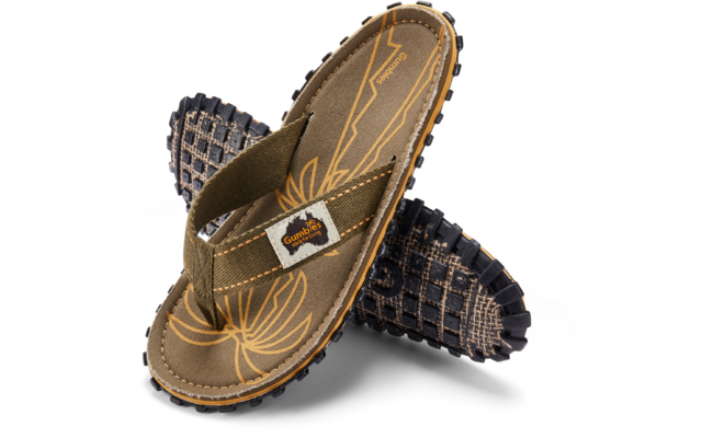 Two crossed olive-green flip-flops; footbeds with yellow curved-line pattern; woven straps with rectangular 'Gumbies' label; black treaded rubber soles
