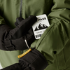Hände mit schwarzen Handschuhen halten eine grüne Jacke und eine weiße Skiauszeichnung