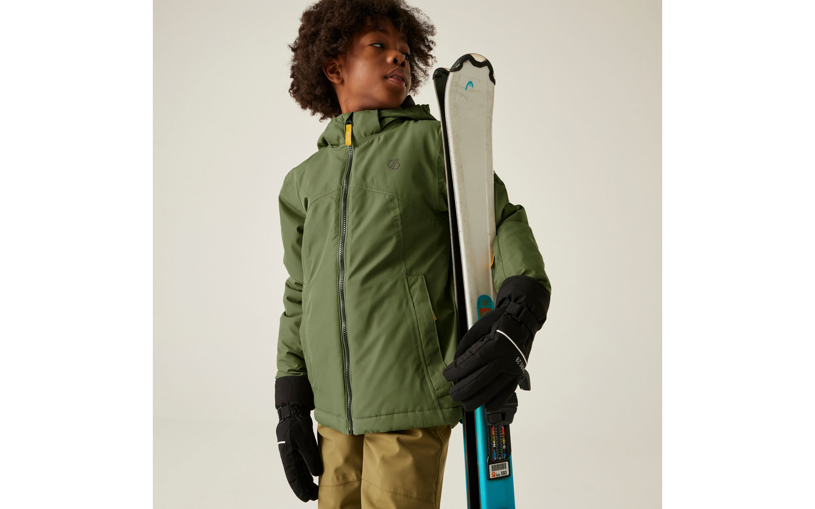 Person mit grüner Jacke hält Skier in der rechten Hand