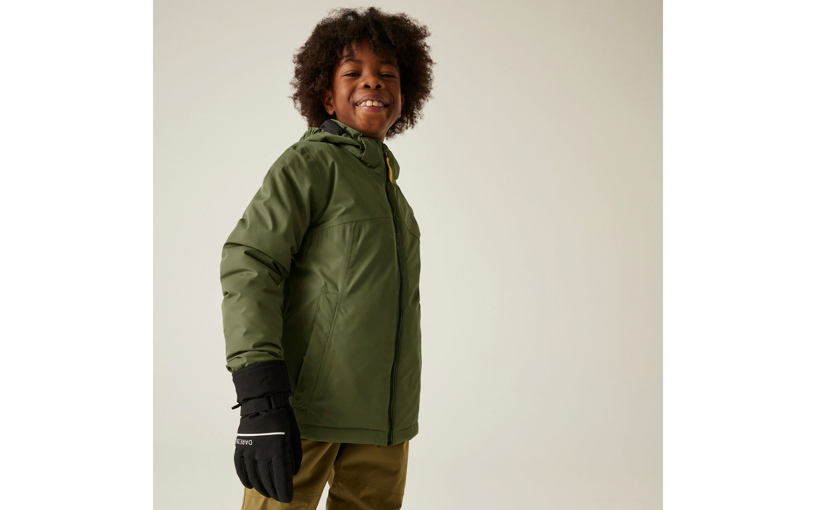 Kind mit lockigen Haaren trägt grüne Jacke und schwarze Handschuhe
