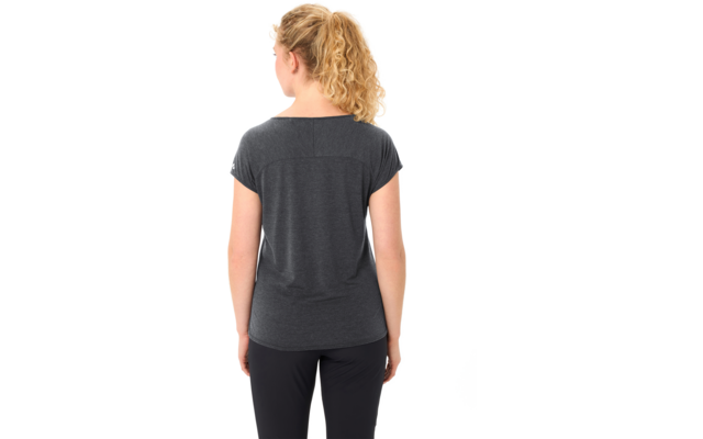 Person von hinten, blondes lockiges Haar zu einem Pferdeschwanz gebunden, trägt dunkelgraues T‑Shirt mit kurzen Ärmeln und schwarze Hose, weißer Hintergrund