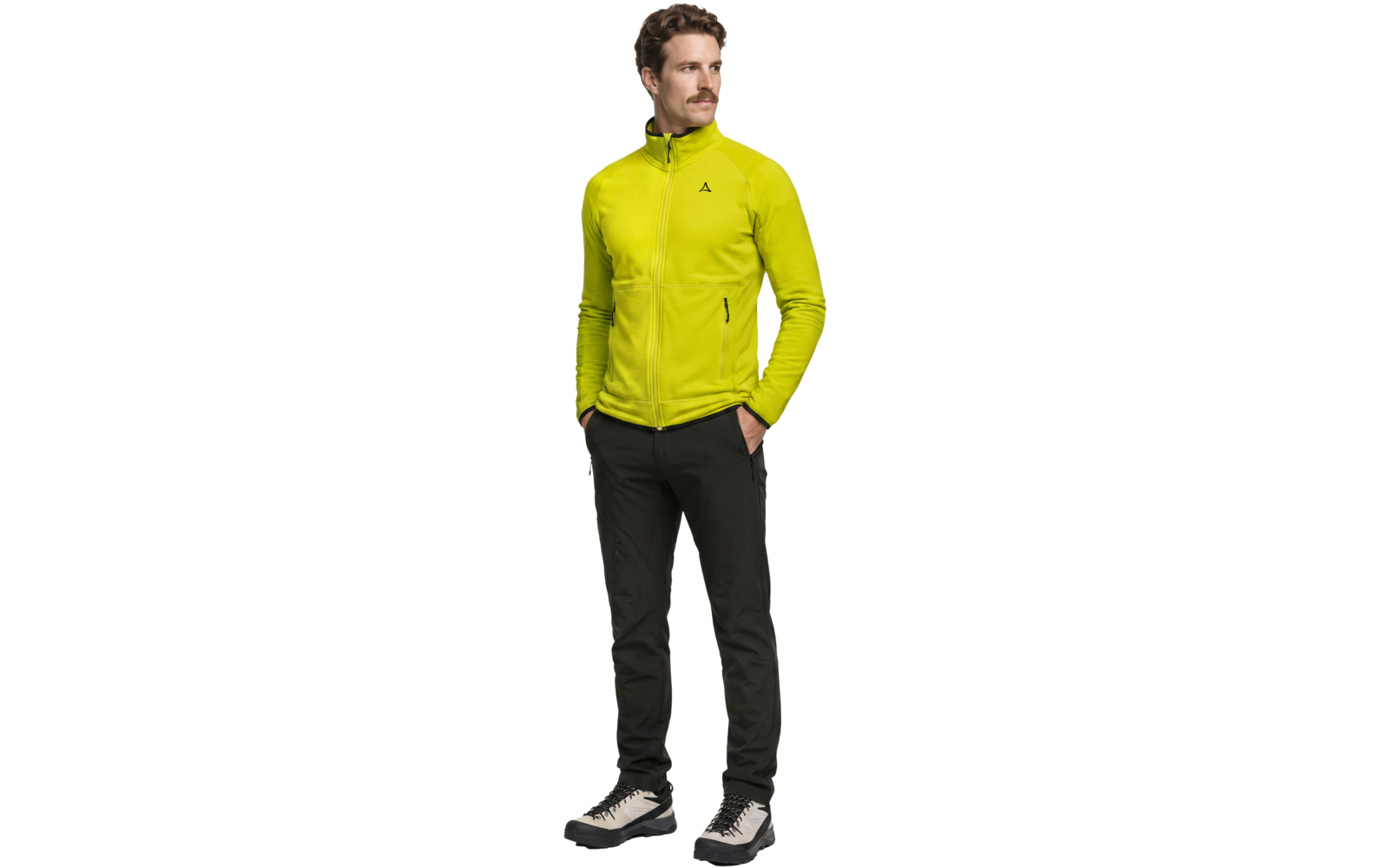 Ganzkörperaufnahme einer Person in gelber Fleecejacke mit Reißverschluss und kleinem Logo, schwarzen Hosen und weißen Sneakers, Hände in den Taschen, schaut nach rechts