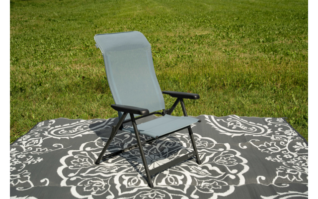 Grauer Klappstuhl mit gepolsterter Rückenlehne und schwarzem Gestell auf einem grau-weißen, floral gemusterten Teppich auf einer Grasfläche