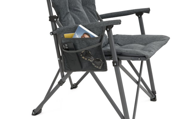 Gepolsterter Klappstuhl mit Armlehnen und seitlicher Netztasche, darin ein Heft mit Porträtfoto, eine Sonnenbrille, eine kleine gelbe Karte und ein schwarzer rechteckiger Gegenstand