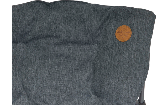 Grauer Stoff mit Falten, brauner runder Lederaufnäher oben rechts, Metallgestell unten rechts sichtbar