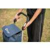 Hands of a person on the handle of a blue shopping trolley with an open flap, grass in the background