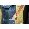 Hand places white water bottle into side pocket of a blue shopping trolley on grass, visible legs and metal frame