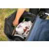 Open black stroller storage with an outstretched arm, folded white-and-red patterned blanket, green handle, beige book and round white object; grass in the background