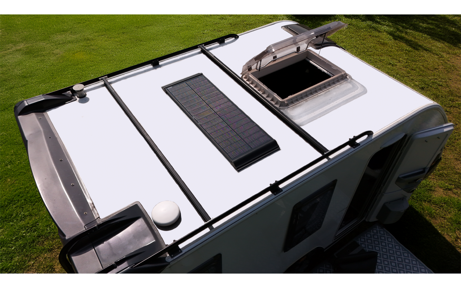 Weißes Wohnmobil von oben mit geöffnetem Dachfenster, auf grünem Rasen