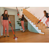 Trois femmes en hauts noirs et pantalons roses utilisent des aspirateurs-balais rouges dans une pièce lumineuse avec escalier en bois et parquet