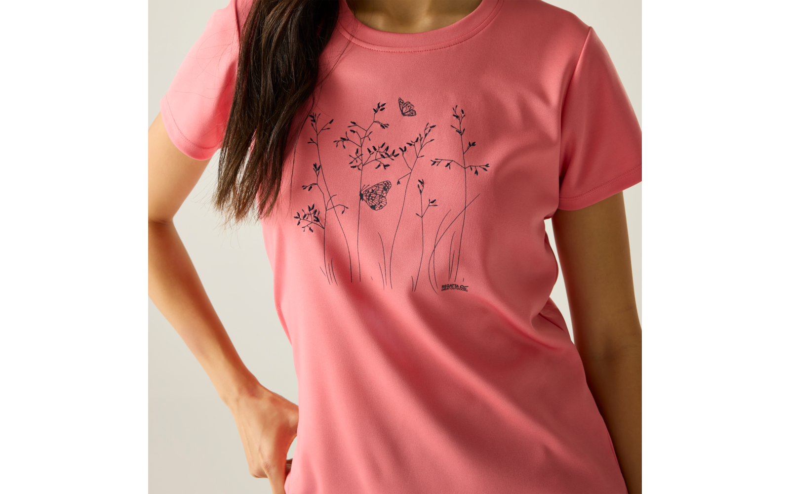 Buste d'une personne portant un t‑shirt rose corail avec un dessin au trait noir de fleurs et de papillons ; visage non visible