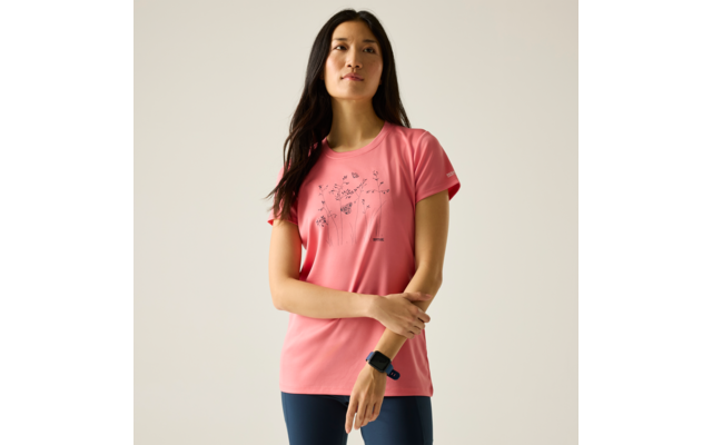Femme debout devant un fond clair, portant un t‑shirt rose à motif floral, un legging bleu foncé et une montre connectée au poignet gauche