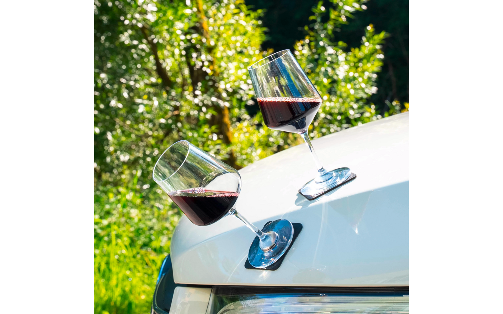 Deux verres de vin rouge sur le capot d'une voiture blanche en plein air