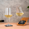 Deux verres à vin avec du vin blanc, un posé sur un dessous de verre, l'autre incliné sur un plateau en bois