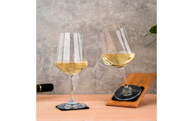 Deux verres à vin avec du vin blanc, un posé sur un dessous de verre, l'autre incliné sur un plateau en bois