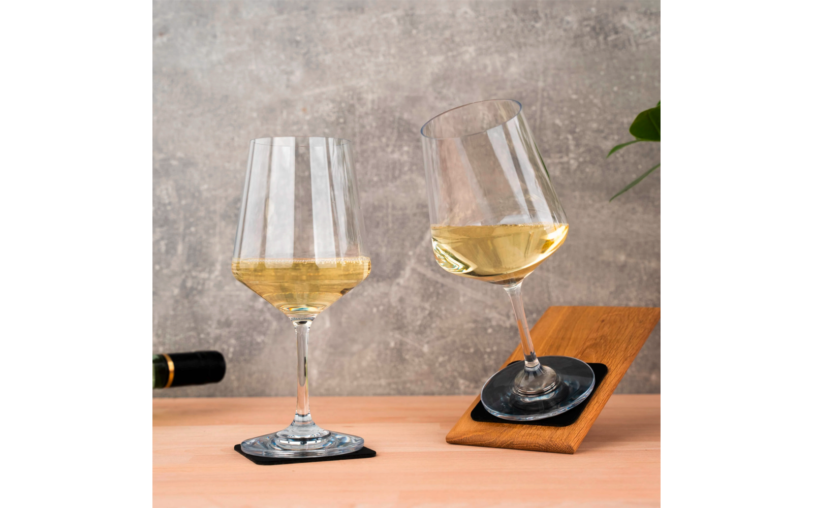 Deux verres à vin avec du vin blanc, un posé sur un dessous de verre, l'autre incliné sur un plateau en bois