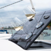Trois verres à vin avec du vin blanc posés sur une surface en verre inclinée sur un bateau, des voiliers visibles en arrière-plan