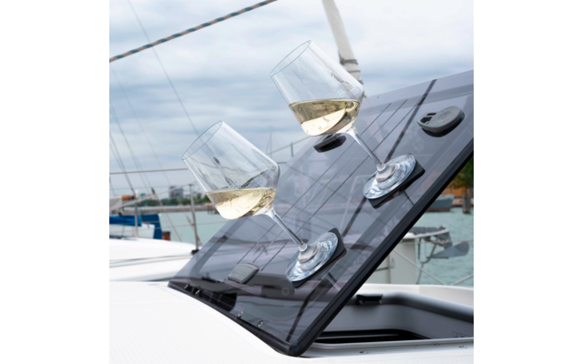 Trois verres à vin avec du vin blanc posés sur une surface en verre inclinée sur un bateau, des voiliers visibles en arrière-plan