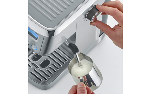 Hand dreht Drehknopf an Espressomaschine; Dampfdüse im Edelstahl-Milchkännchen mit sichtbarem Milchschaum