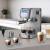 Edelstahl-Espressomaschine auf Küchenarbeitsplatte, zwei Espressotassen unter dem Siebträger, weitere geschichtete Kaffees in Gläsern, Tamper, Filtereinsätze und Dampfdüse sichtbar