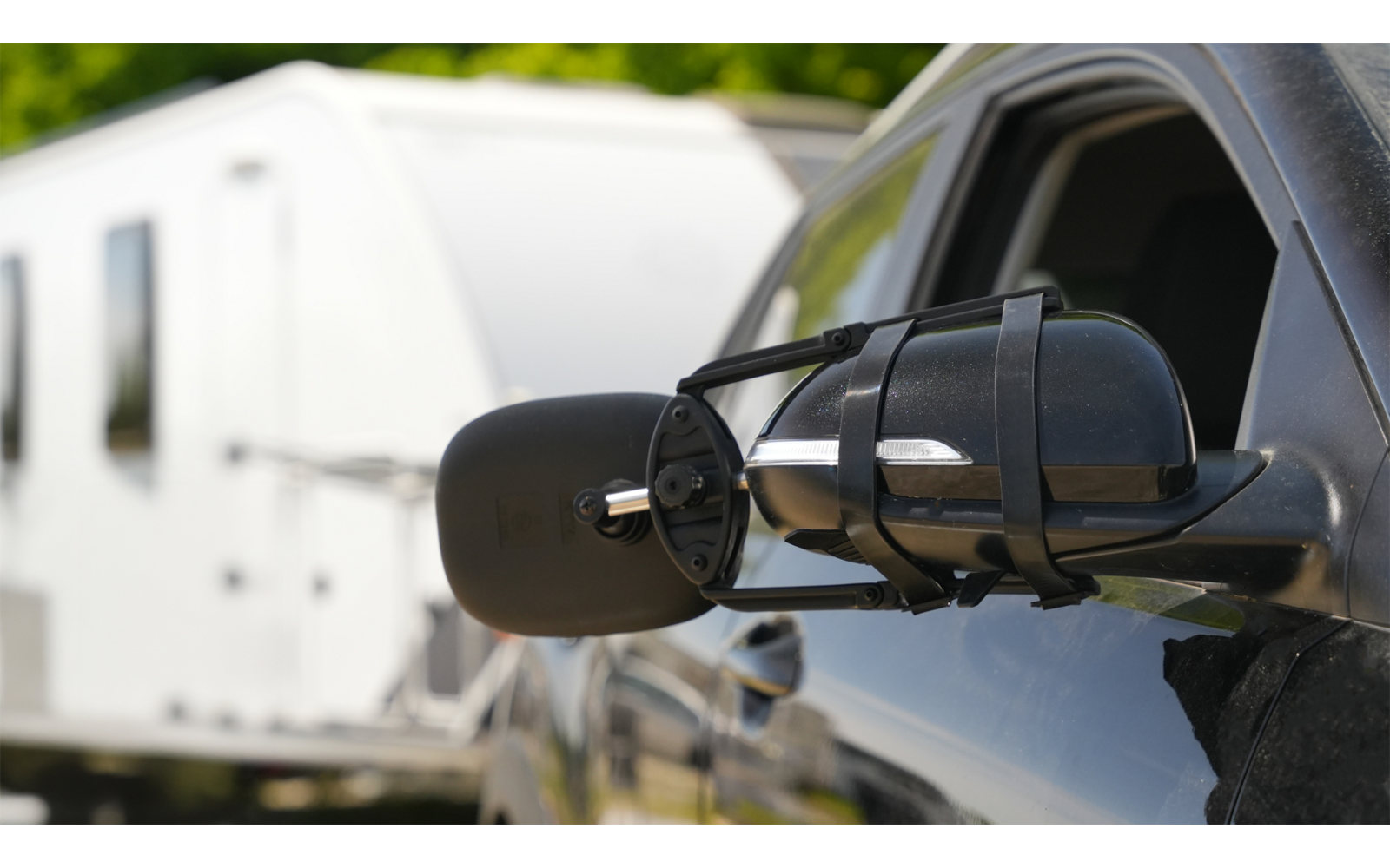 Seitenspiegel eines schwarzen Fahrzeugs mit einem weißen Wohnwagen im Hintergrund
