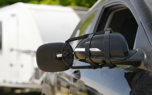 Espejo lateral de un vehículo negro con una caravana blanca al fondo
