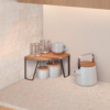 Küchenarbeitsplatte mit kleinem Holzregal, zwei Glasbechern, einer weißen Tasse, zwei weißen Vorratsdosen mit Holzdeckeln darunter und einem weißen Wasserkocher mit Holzdeckel