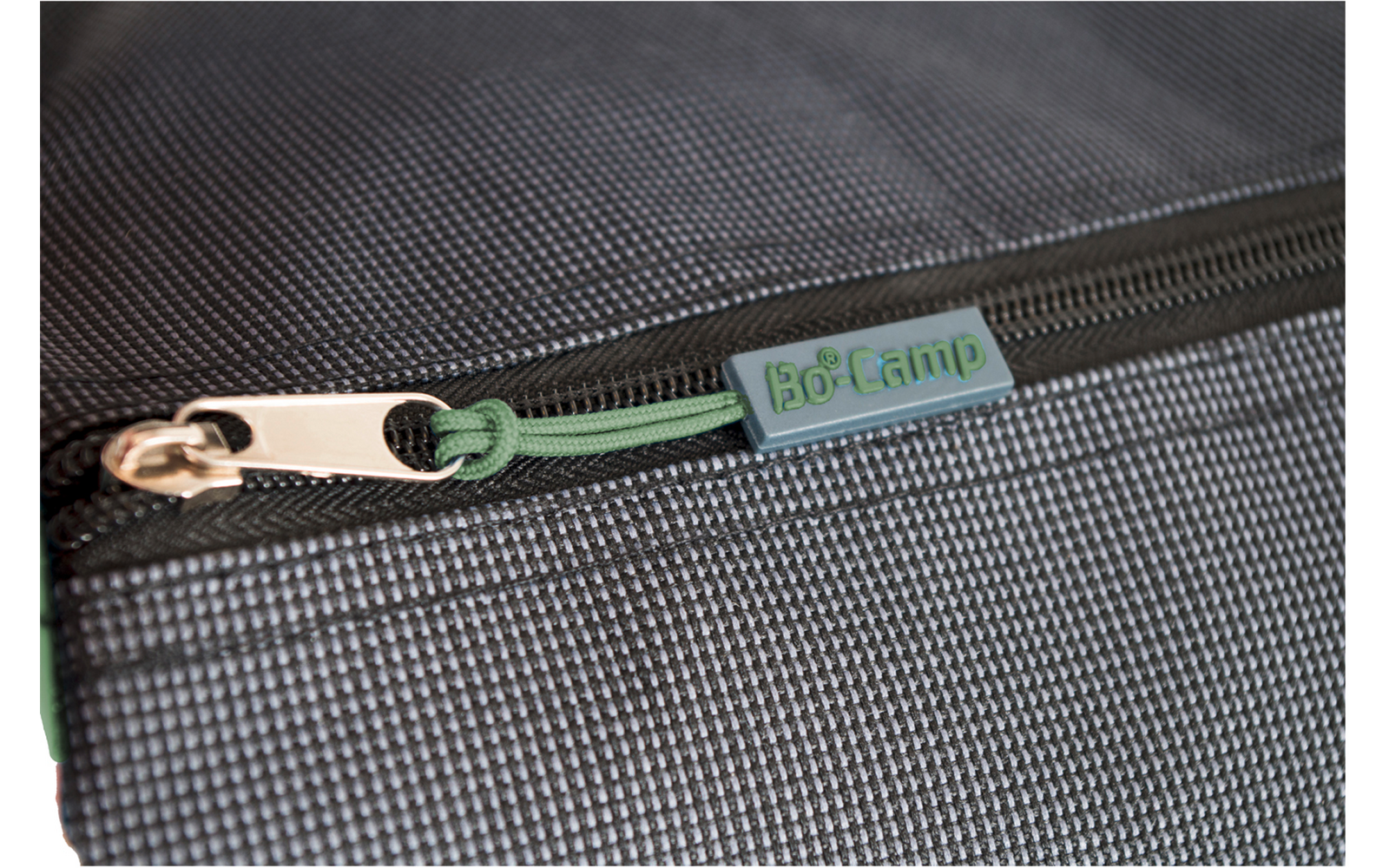 Gros plan d'une fermeture éclair avec curseur métallique sur tissu gris texturé ; cordon vert avec étiquette plastique 'Bo-Camp'