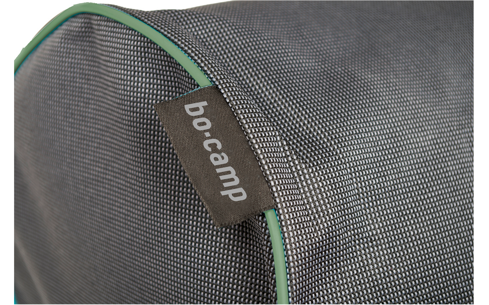 Gros plan sur un tissu gris finement structuré avec passepoil vert et une étiquette en tissu brune avec texte blanc 'bo-camp'
