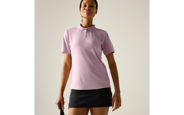 Person mit kurzem dunklem Haar, trägt hellviolettes Poloshirt und kurzen schwarzen Rock, steht vor hellem einfarbigem Hintergrund, hält schwarzen Trageriemen in der linken Hand