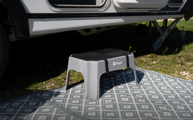 Grauer Kunststofftritt auf gemusterter Außenmatte vor einem Wohnwagen, Gras im Hintergrund