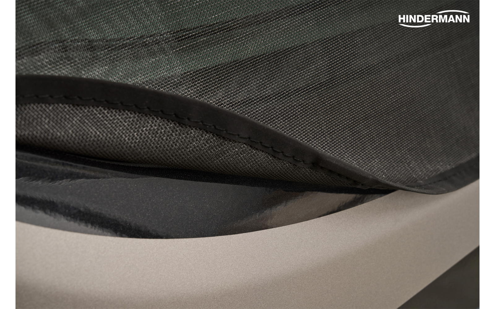 Primo piano di strati di tessuto sovrapposti nero e grigio scuro con cucitura, logo HINDERMANN in alto a destra e superficie liscia grigio chiaro sotto