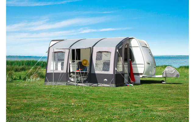 Caravane avec auvent attaché sur une prairie verte, ciel bleu et mer en arrière-plan