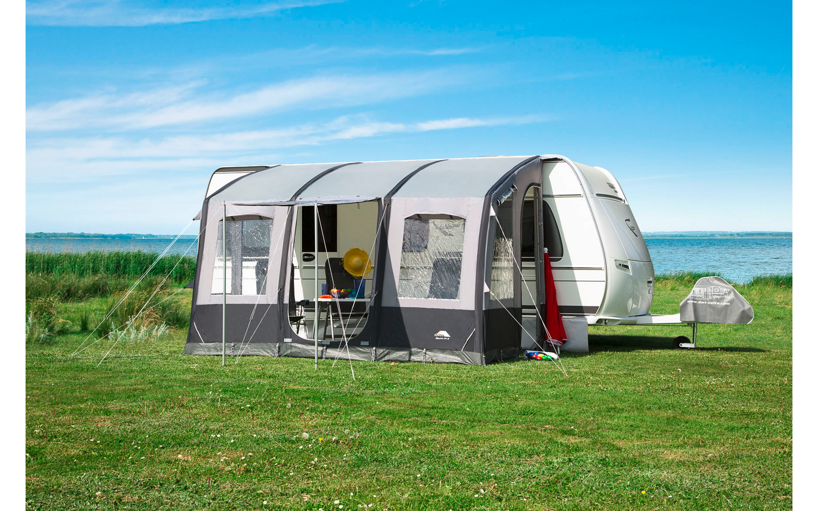 Caravane avec auvent attaché sur une prairie verte, ciel bleu et mer en arrière-plan