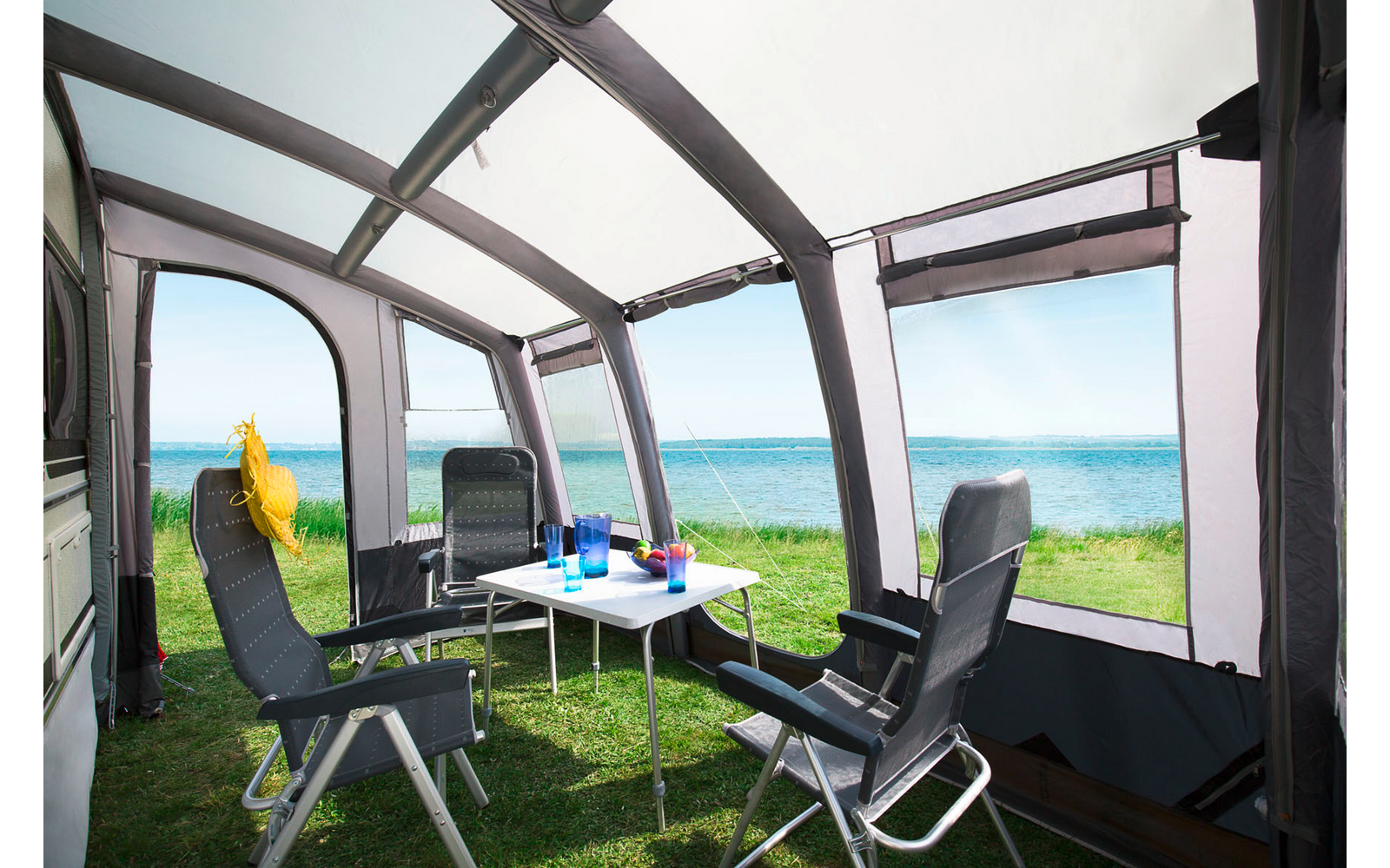 Vue depuis un balcon couvert sur la mer et la côte, avec deux chaises pliantes, une petite table et des boissons