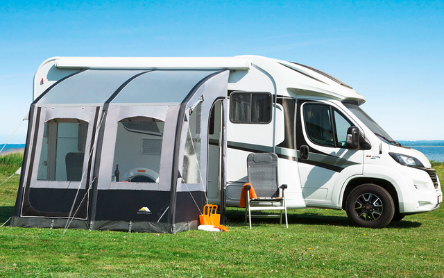 Motorhome with attached awning on a grassy field under a clear sky