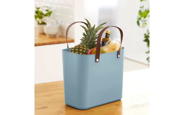 Blaue Einkaufstasche mit Ananas, Bananen und Blumentopf auf einem Holztisch